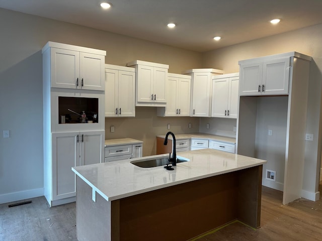 kitchen with white cabinetry, sink, an island with sink, and light stone counters