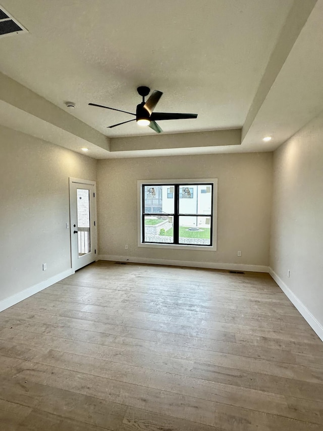 empty room featuring ceiling fan, wood finished floors, and a raised ceiling