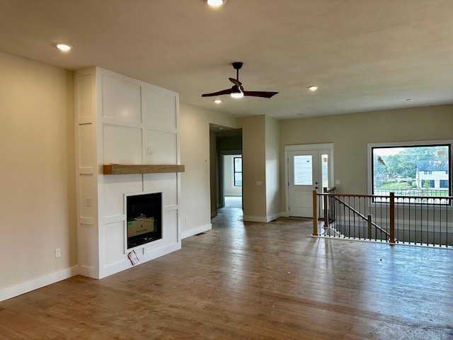 unfurnished living room featuring a ceiling fan, a fireplace, wood finished floors, baseboards, and recessed lighting