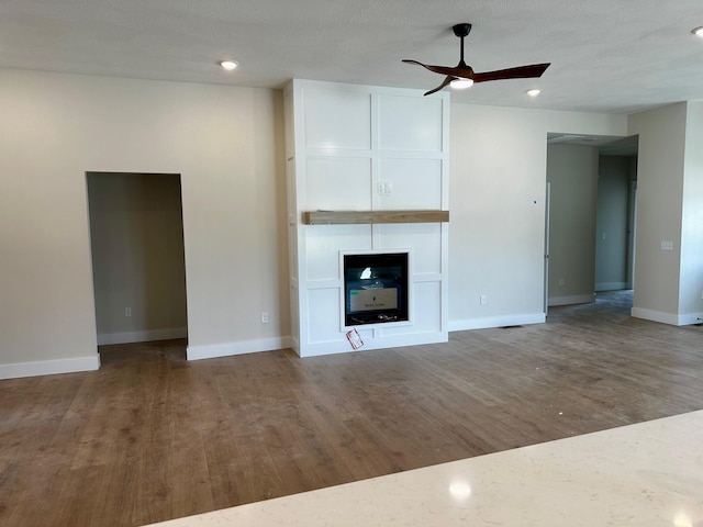 unfurnished living room featuring wood finished floors, baseboards, recessed lighting, a large fireplace, and a ceiling fan