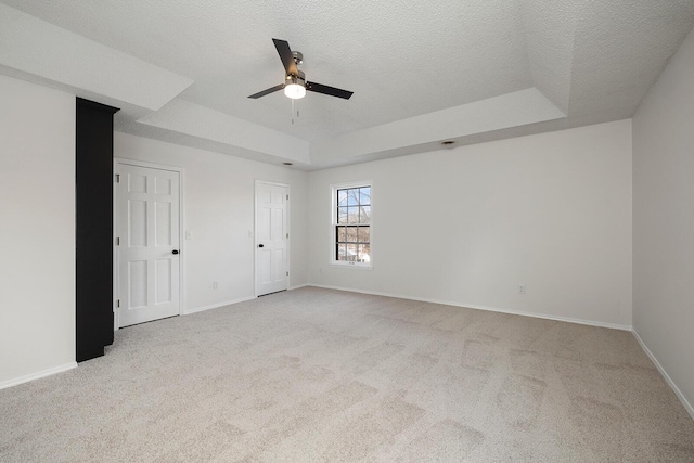 unfurnished bedroom with a tray ceiling, ceiling fan, light colored carpet, and a textured ceiling