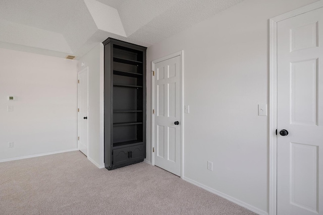 unfurnished bedroom featuring a textured ceiling, light carpet, and vaulted ceiling