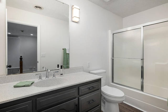 full bathroom with a textured ceiling, vanity, shower / bath combination with glass door, wood-type flooring, and toilet