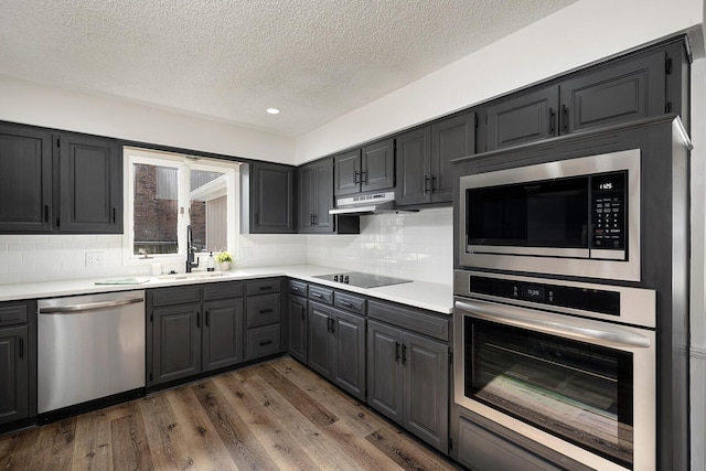 kitchen featuring sink, tasteful backsplash, dark hardwood / wood-style flooring, a textured ceiling, and appliances with stainless steel finishes