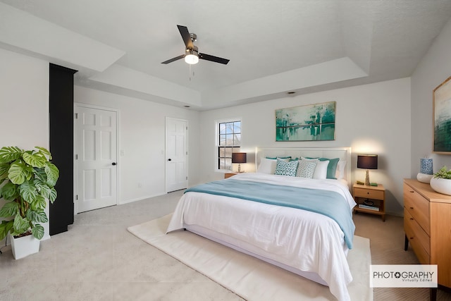 carpeted bedroom with ceiling fan and a tray ceiling