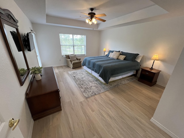 bedroom with light hardwood / wood-style floors, a raised ceiling, and ceiling fan