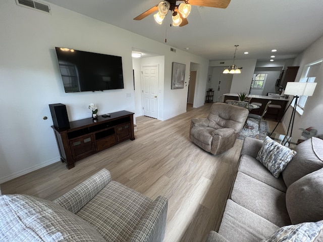 living room with ceiling fan with notable chandelier and light wood-type flooring