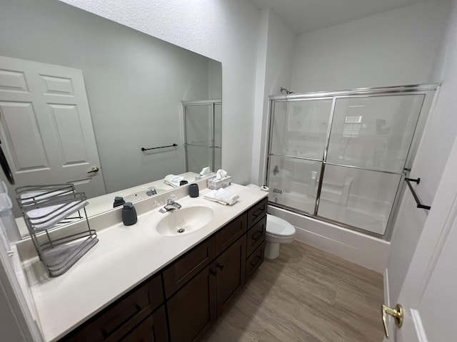 full bathroom with vanity, hardwood / wood-style flooring, toilet, and bath / shower combo with glass door