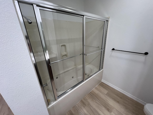 bathroom with shower / bath combination with glass door, hardwood / wood-style flooring, and toilet