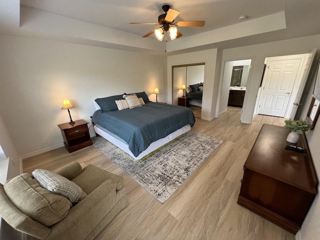 bedroom featuring ensuite bath, ceiling fan, light wood-type flooring, a tray ceiling, and a closet