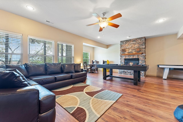 living room featuring hardwood / wood-style floors, a textured ceiling, a stone fireplace, and ceiling fan