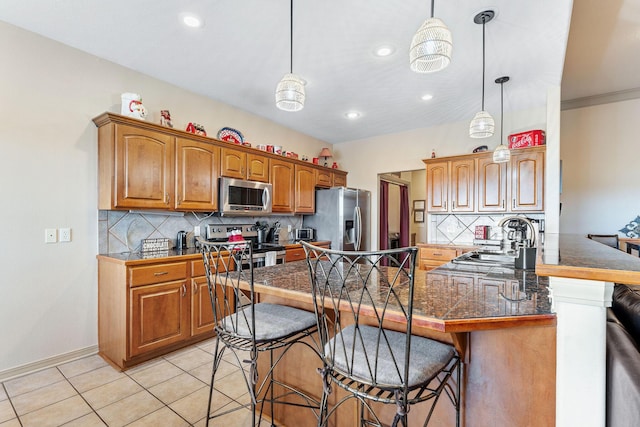 kitchen featuring kitchen peninsula, appliances with stainless steel finishes, a breakfast bar, sink, and hanging light fixtures