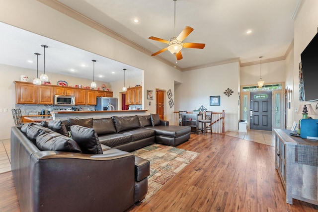 living room with a high ceiling, light hardwood / wood-style flooring, ceiling fan, and ornamental molding