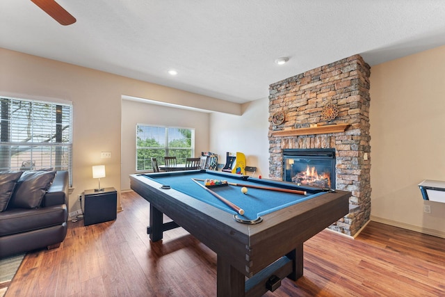 rec room with hardwood / wood-style flooring, a stone fireplace, a textured ceiling, and pool table