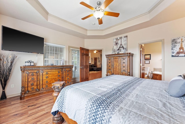 bedroom featuring a tray ceiling, ensuite bathroom, light hardwood / wood-style flooring, and ceiling fan