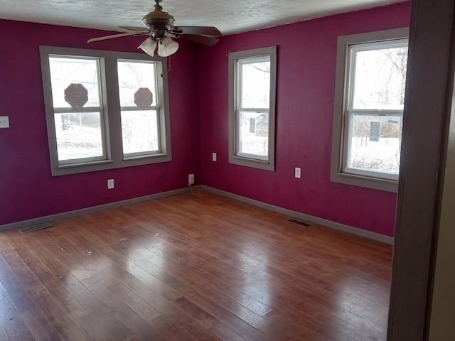 unfurnished room featuring baseboards, wood finished floors, visible vents, and a healthy amount of sunlight