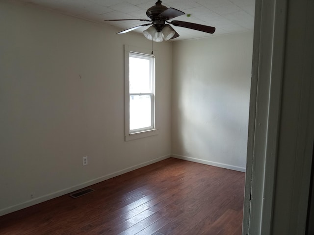 empty room with dark wood-style floors, visible vents, a ceiling fan, and baseboards