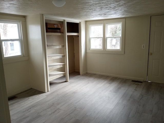 unfurnished bedroom with a closet, a textured ceiling, baseboards, and wood finished floors