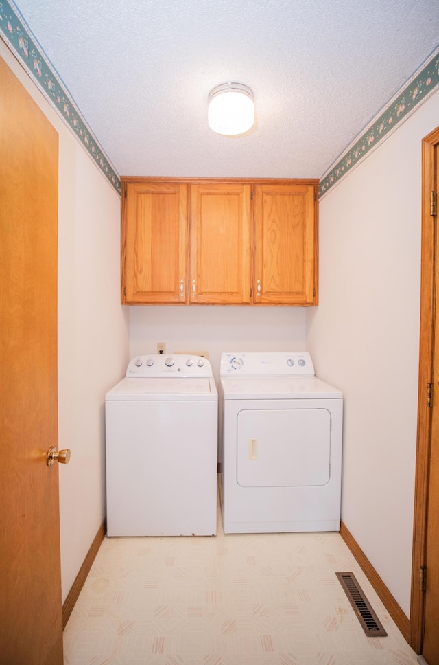 washroom with washing machine and clothes dryer, cabinets, and a textured ceiling