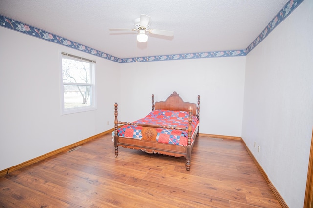 bedroom with ceiling fan, wood-type flooring, and a textured ceiling