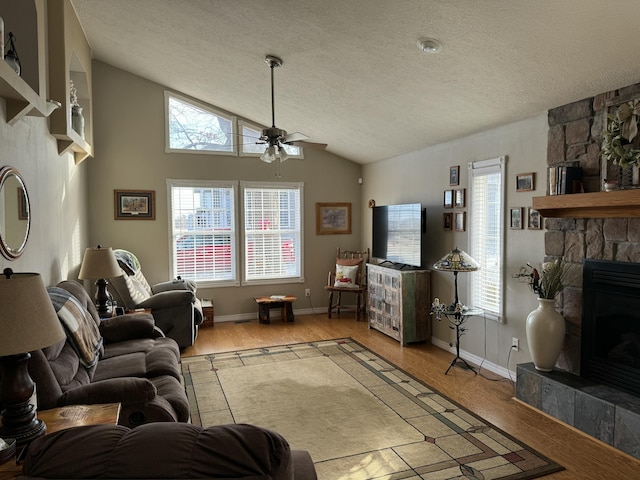 living room with a stone fireplace, vaulted ceiling, ceiling fan, light wood-type flooring, and a textured ceiling