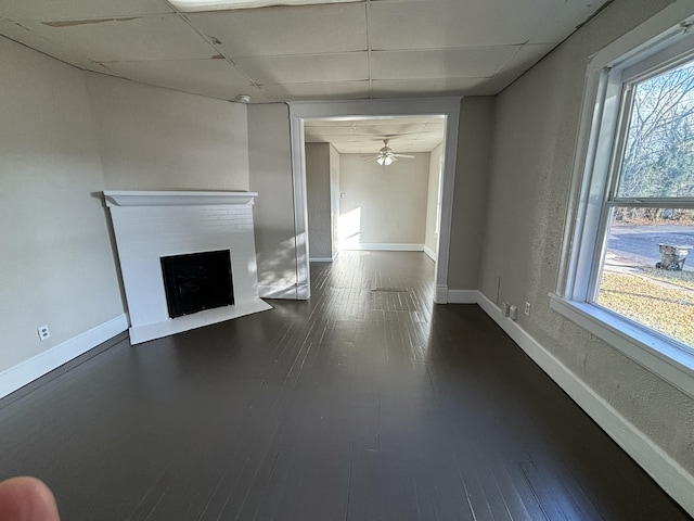 unfurnished living room featuring ceiling fan, a drop ceiling, and dark wood-type flooring