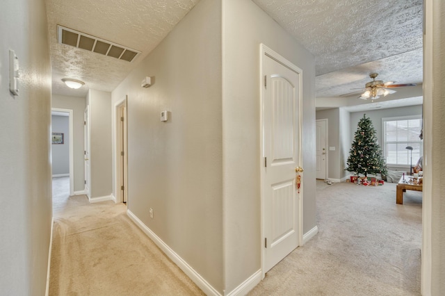 hallway with light carpet and a textured ceiling