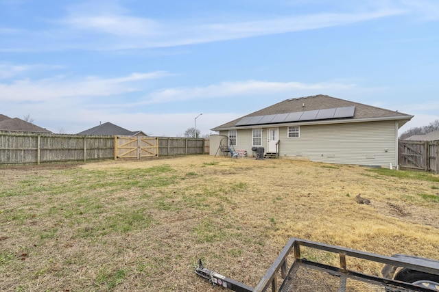 rear view of house featuring solar panels, a yard, a fenced backyard, and a gate