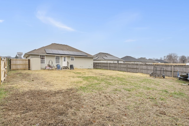 back of house featuring a fenced backyard, roof mounted solar panels, and a lawn