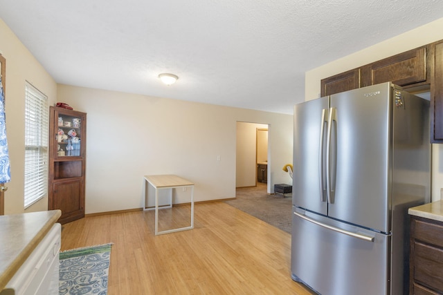 kitchen featuring dark brown cabinetry, baseboards, freestanding refrigerator, light countertops, and light wood-type flooring