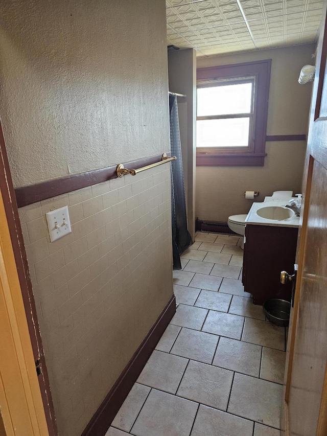 bathroom with tile walls, toilet, vanity, and tile patterned flooring