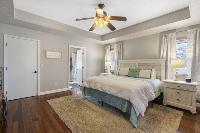 bedroom with ceiling fan, dark hardwood / wood-style floors, ensuite bath, and a tray ceiling