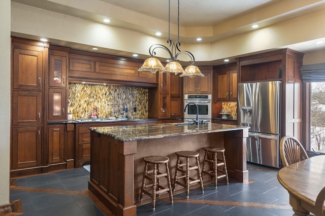 kitchen featuring pendant lighting, a kitchen island with sink, dark stone countertops, a kitchen bar, and stainless steel appliances