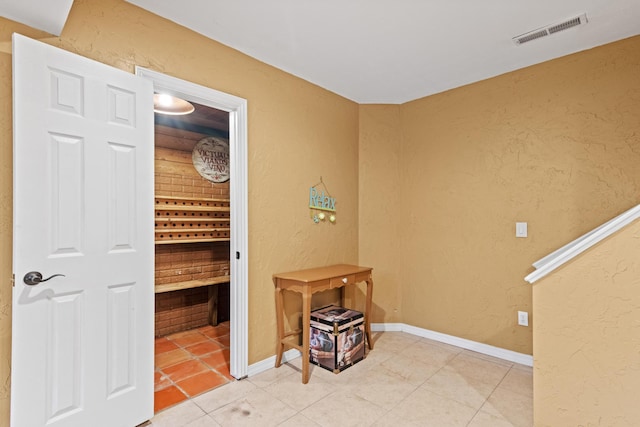 hall with light tile patterned flooring, baseboards, visible vents, and a textured wall
