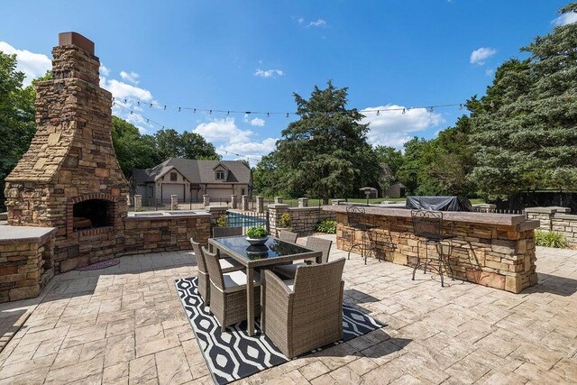 view of patio featuring an outdoor stone fireplace, fence, and outdoor dry bar
