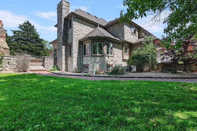 view of property exterior featuring fence, stone siding, a gate, a chimney, and a lawn