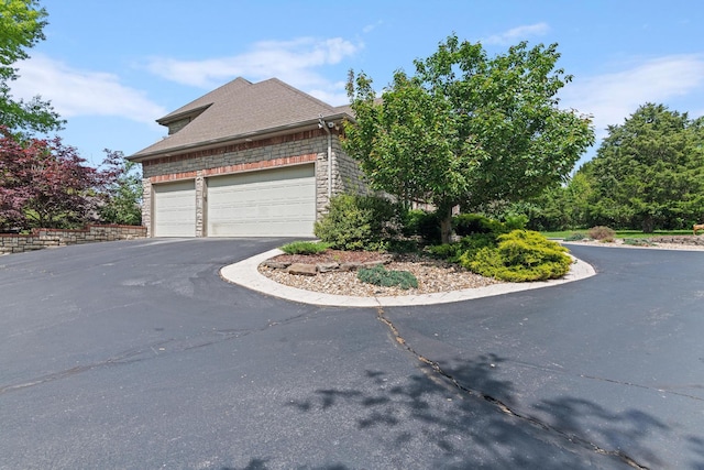 view of property exterior featuring an attached garage, driveway, and stone siding