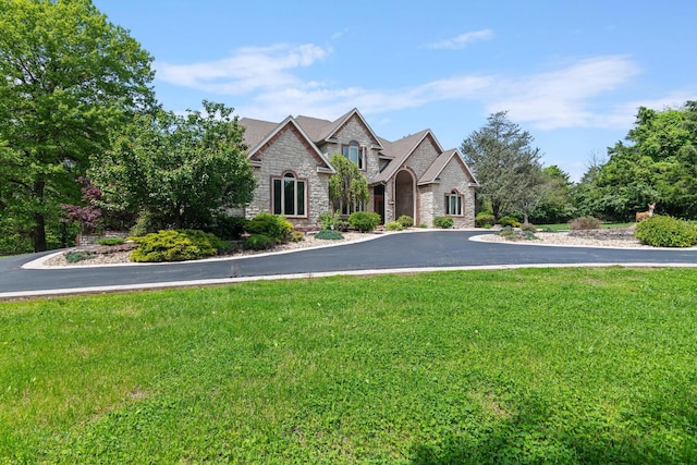 view of front facade with curved driveway, stone siding, and a front lawn