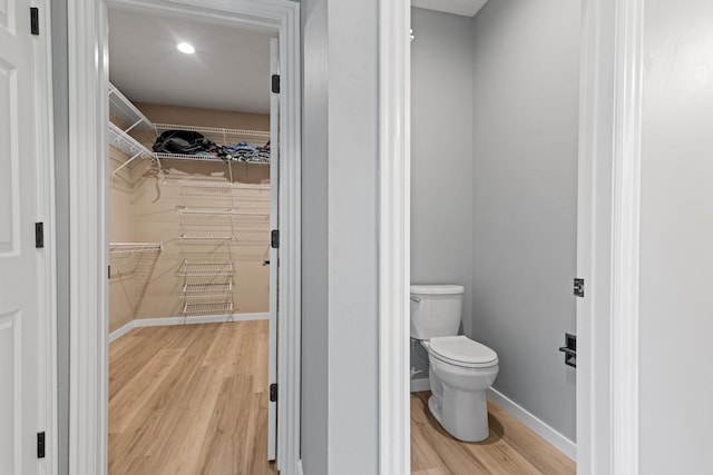 bathroom with wood finished floors, toilet, baseboards, recessed lighting, and a spacious closet