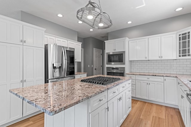 kitchen featuring a kitchen island, white cabinets, light wood finished floors, appliances with stainless steel finishes, and backsplash