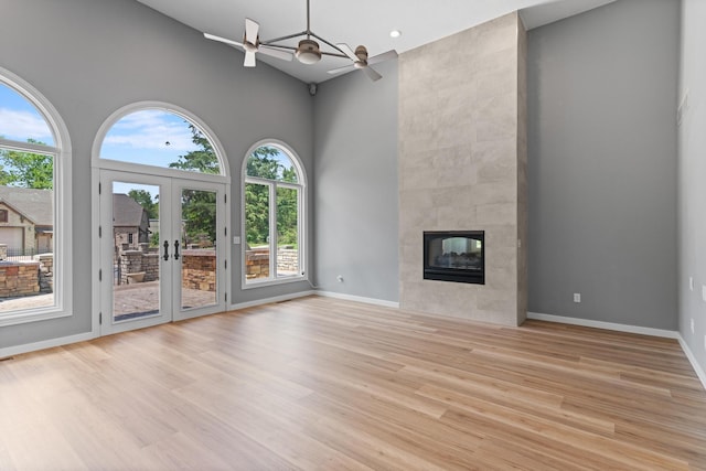 unfurnished living room featuring a fireplace, baseboards, a high ceiling, french doors, and light wood finished floors