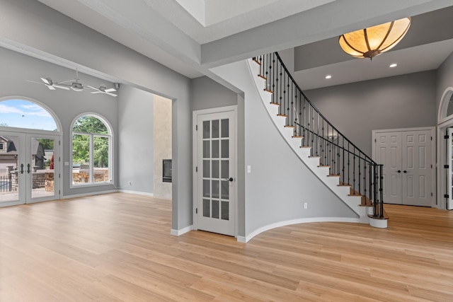 entrance foyer with french doors, a towering ceiling, baseboards, light wood-style floors, and stairs