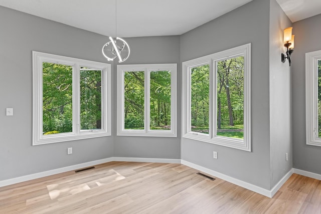 unfurnished dining area featuring a chandelier, baseboards, visible vents, and light wood-style floors