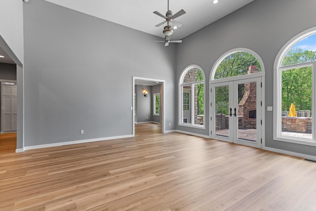empty room featuring baseboards, a ceiling fan, light wood finished floors, and high vaulted ceiling
