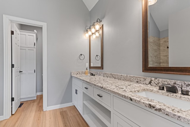 bathroom with wood finished floors, a sink, lofted ceiling, and double vanity