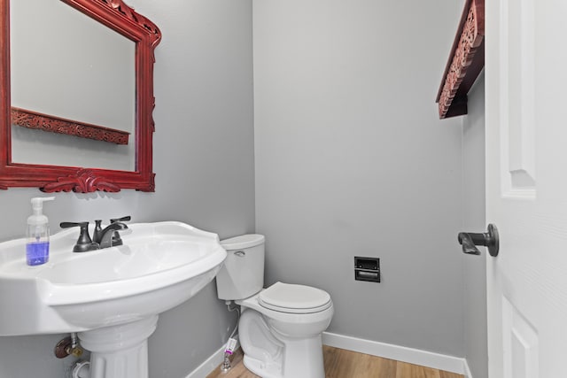 half bathroom with a sink, baseboards, toilet, and wood finished floors