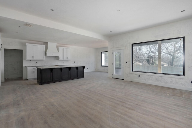 kitchen with white cabinetry, a center island, wall chimney range hood, and light hardwood / wood-style floors