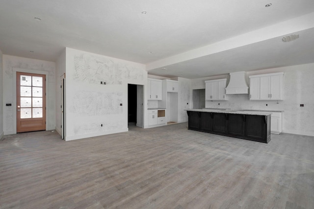 kitchen with wall chimney range hood, light hardwood / wood-style floors, a center island, and white cabinets