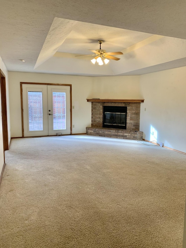 unfurnished living room with ceiling fan, a textured ceiling, a tray ceiling, a fireplace, and carpet