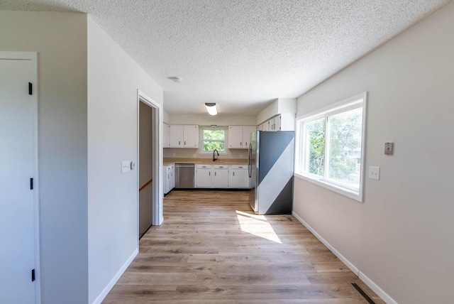 kitchen featuring white cabinets, sink, light wood-type flooring, a textured ceiling, and stainless steel appliances